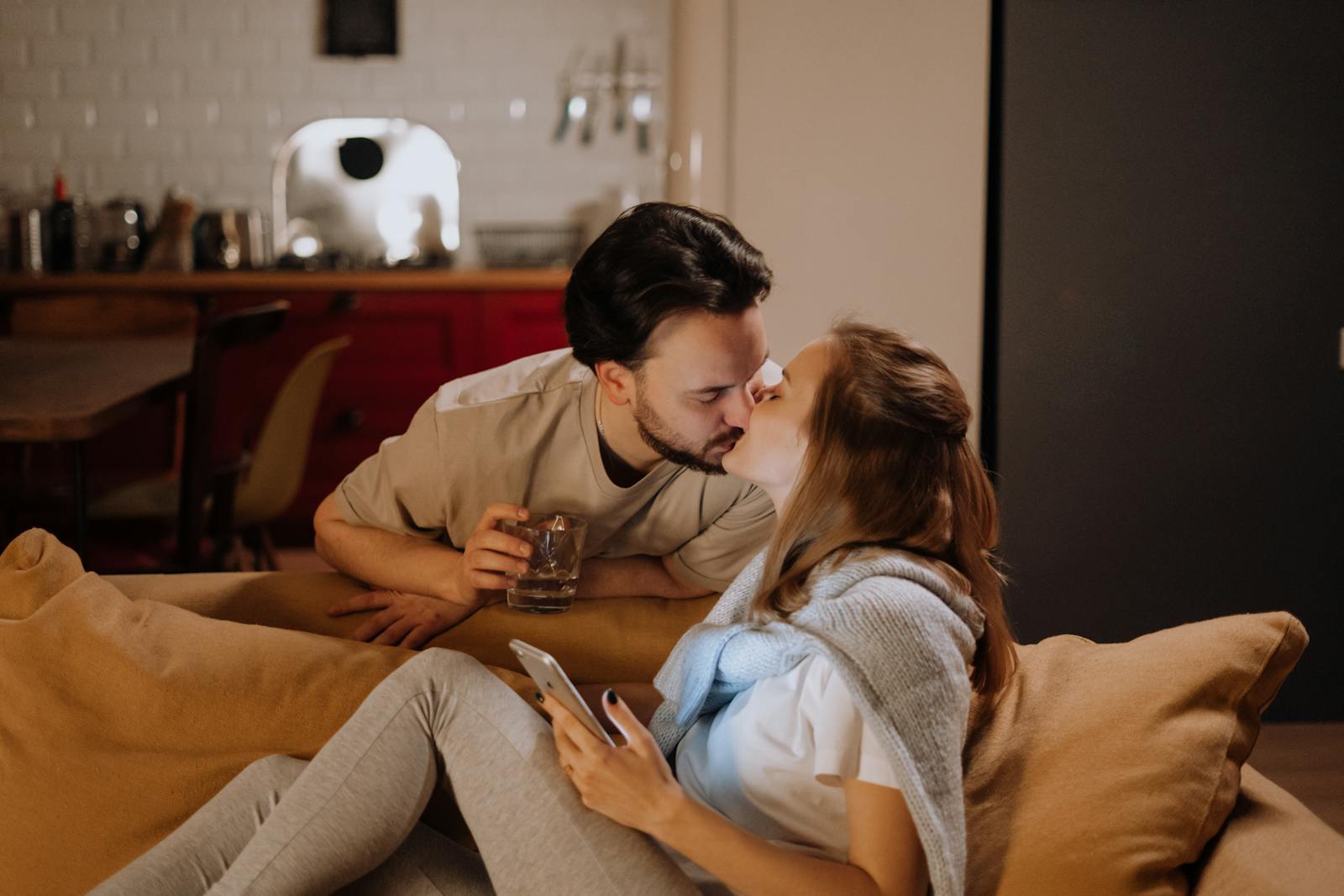 A couple sharing a tender kiss on the couch in a cozy living room setting.