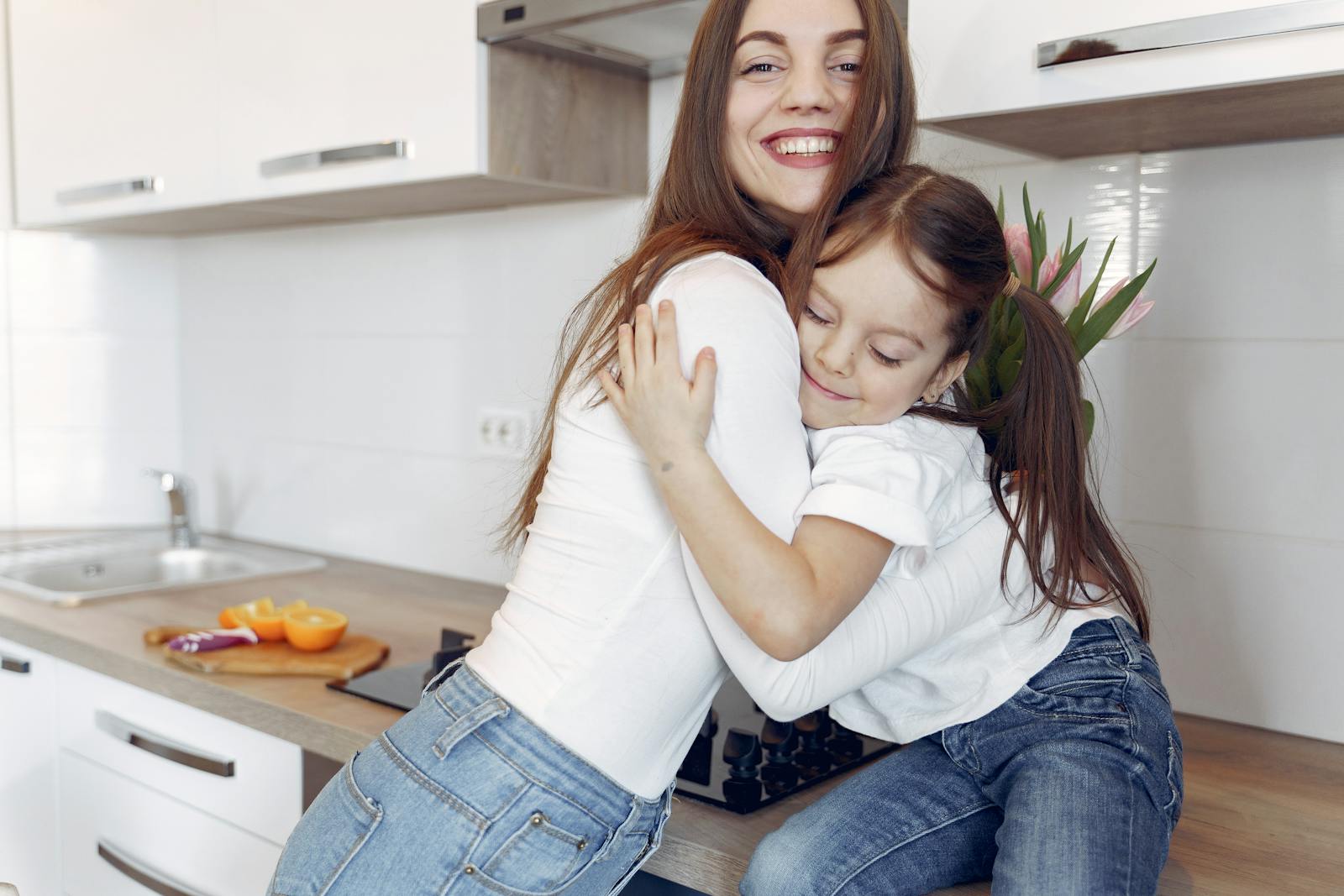 A joyful moment of a mother and daughter hugging in a modern kitchen setting.