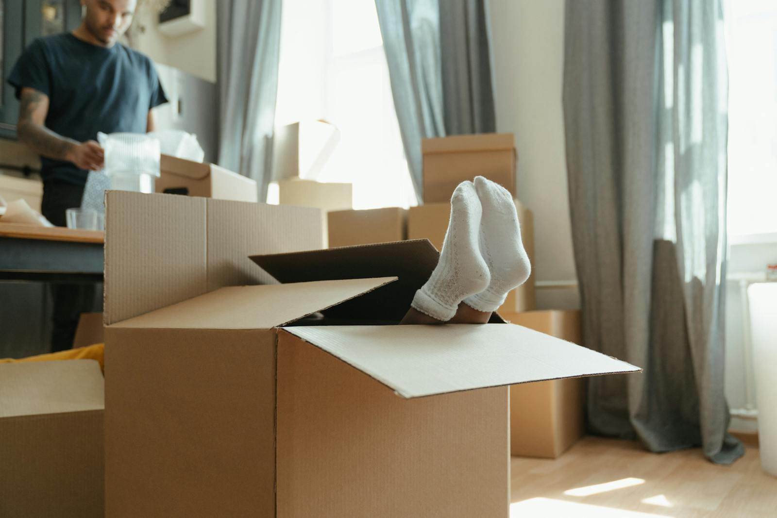A playful scene of feet sticking out of a cardboard box during moving day in a bright, indoor setting.