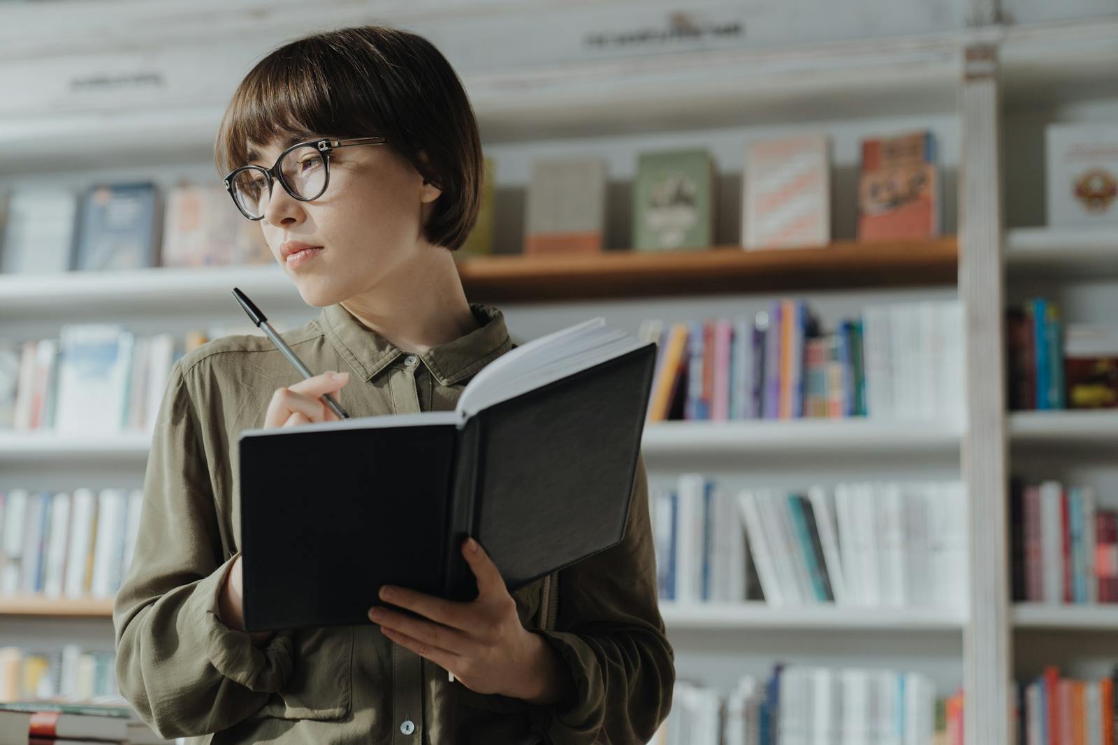 Focused woman taking notes in a bookstore, surrounded by shelves of books, fostering learning.