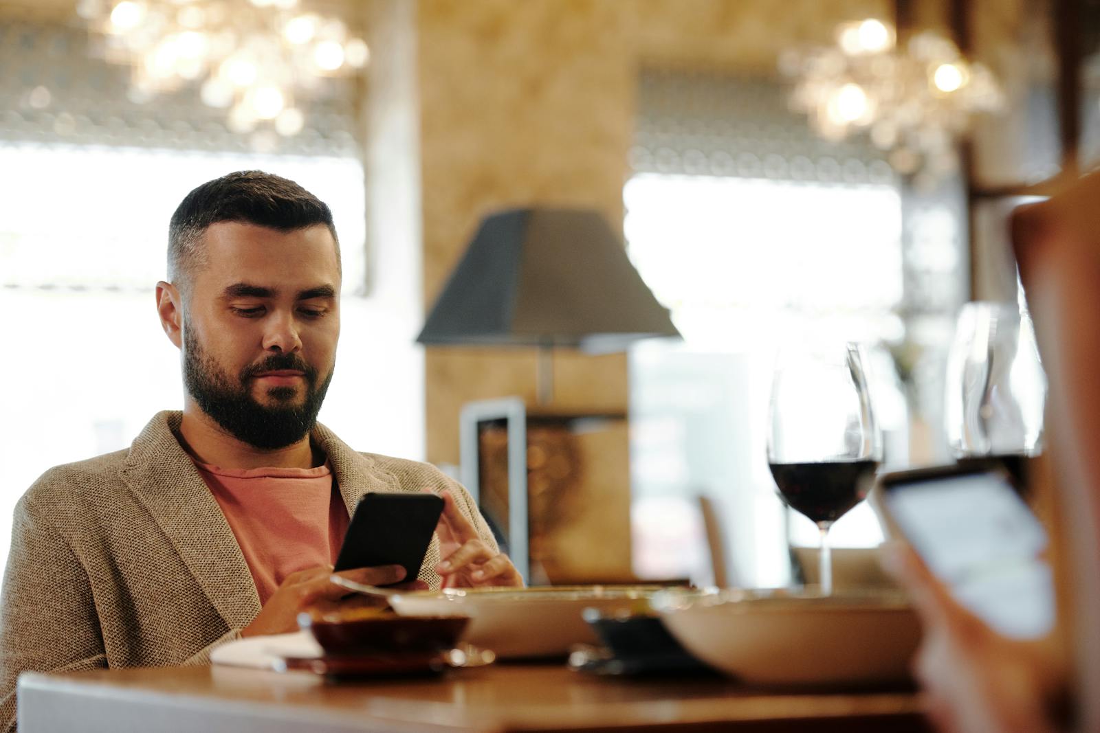 Man with smartphone engaging in activity at restaurant table with wine glass.