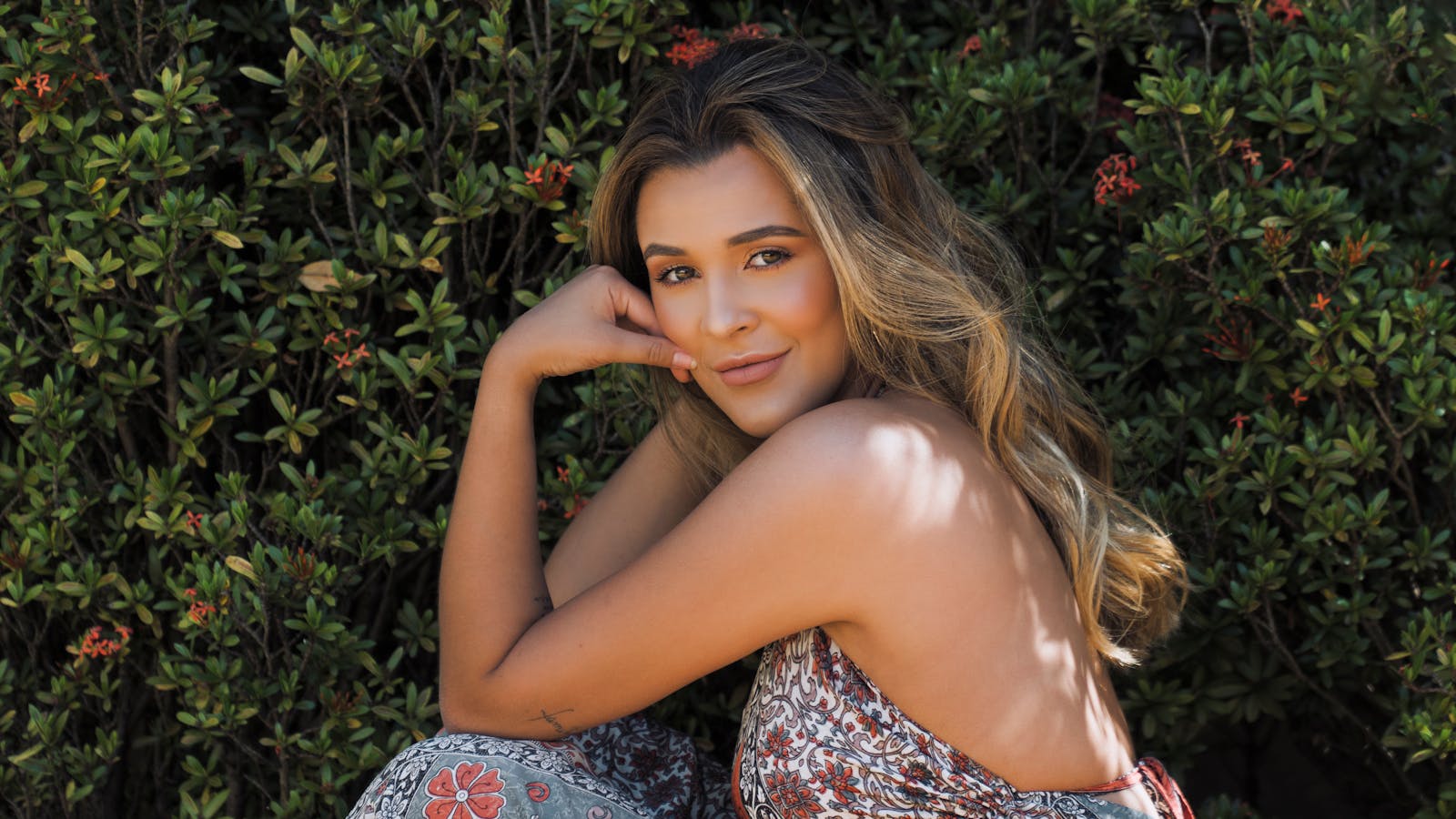 A beautiful young woman posing and smiling next to vibrant bushes outdoors in Brazil.