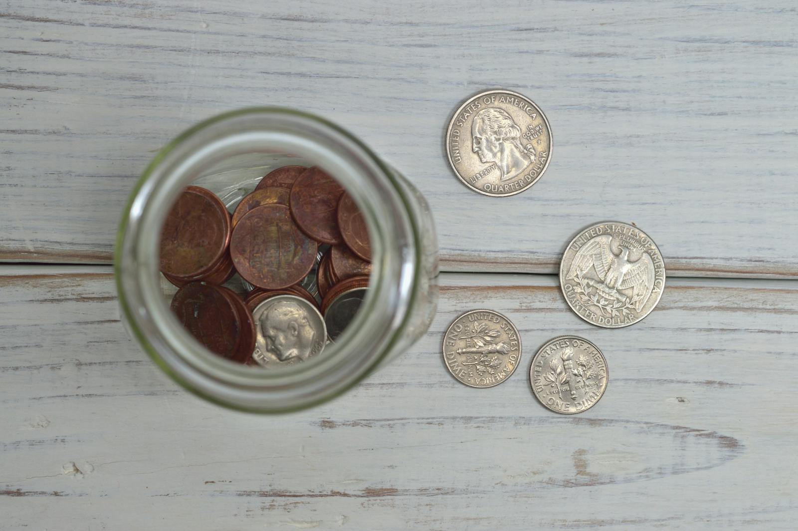 Top view of a jar filled with coins placed on a wooden table, depicting savings.