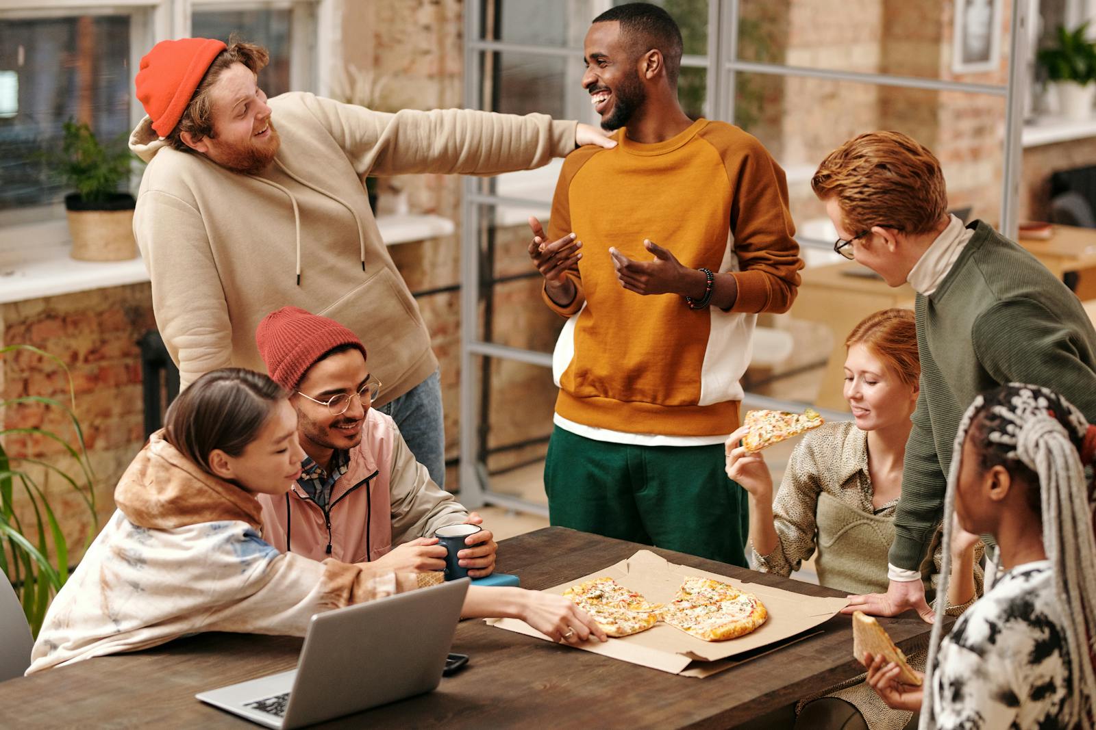 A group of diverse friends laughing and enjoying pizza together indoors.