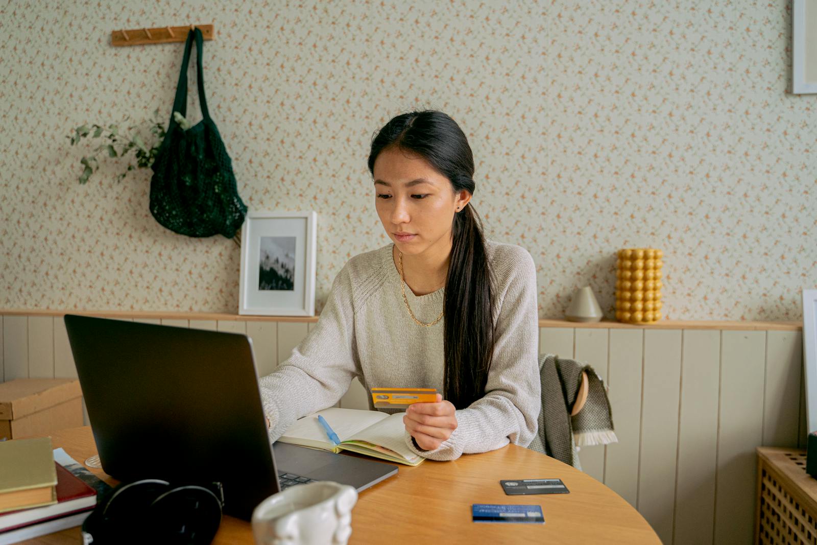 A woman using a laptop and credit card for online shopping at a cozy indoor setting.