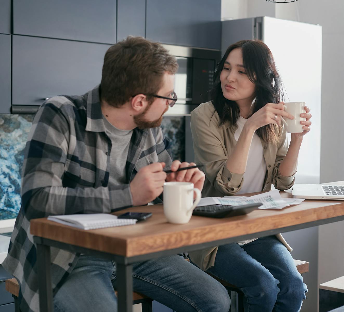 A couple in a cozy kitchen setting reviewing finances with coffee and paperwork.