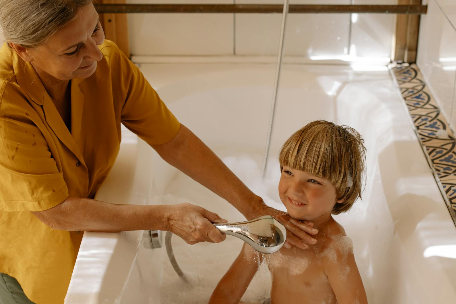 A grandmother gently bathing her grandson in a bright, cozy bathroom.
