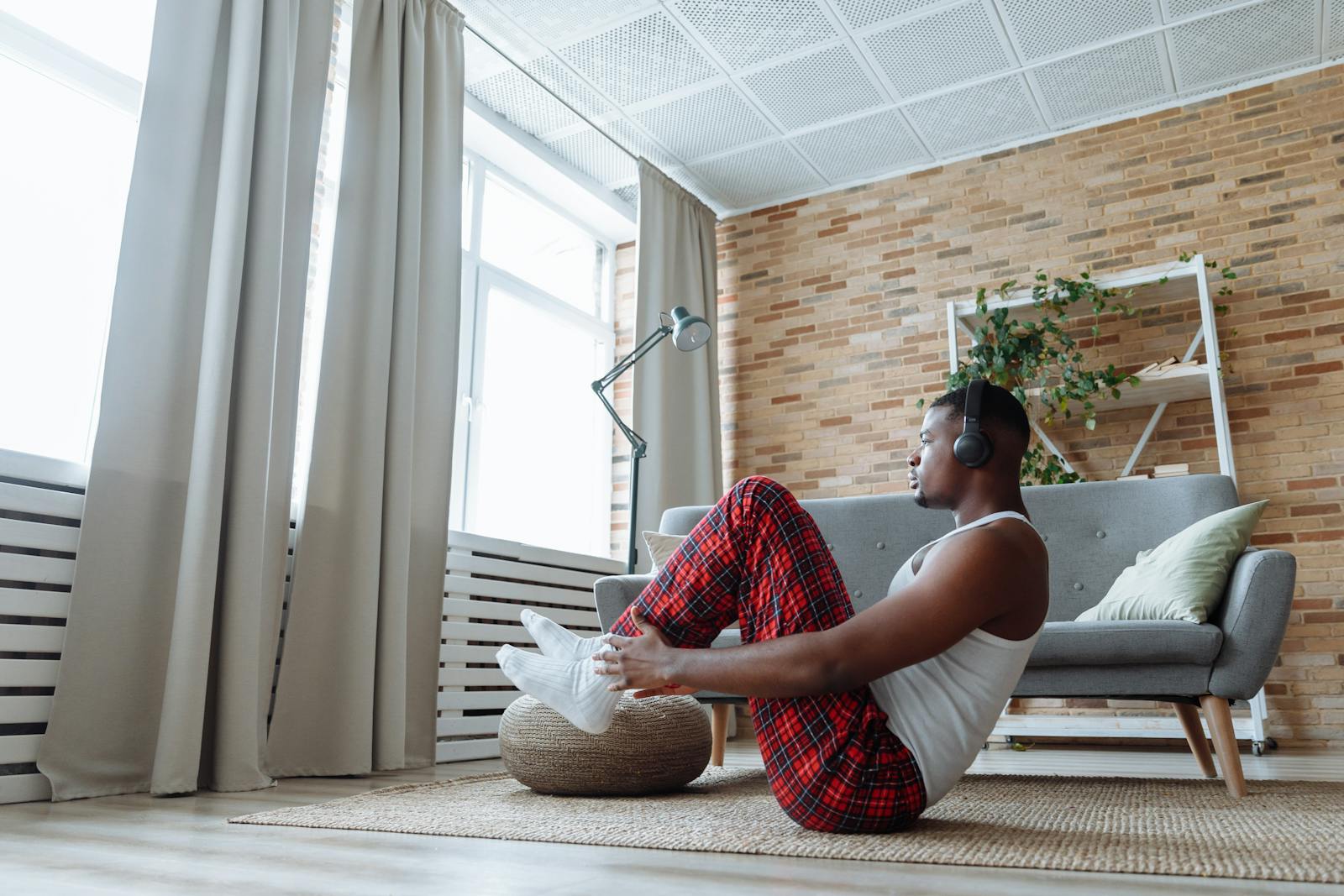 A man performs sit-ups indoors while wearing headphones, surrounded by modern cozy decor.