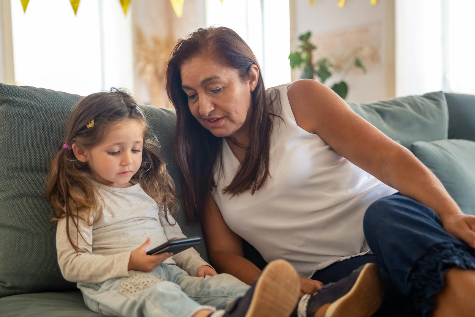 A grandmother and her granddaughter bonding over a smartphone while sitting on a cozy couch indoors.