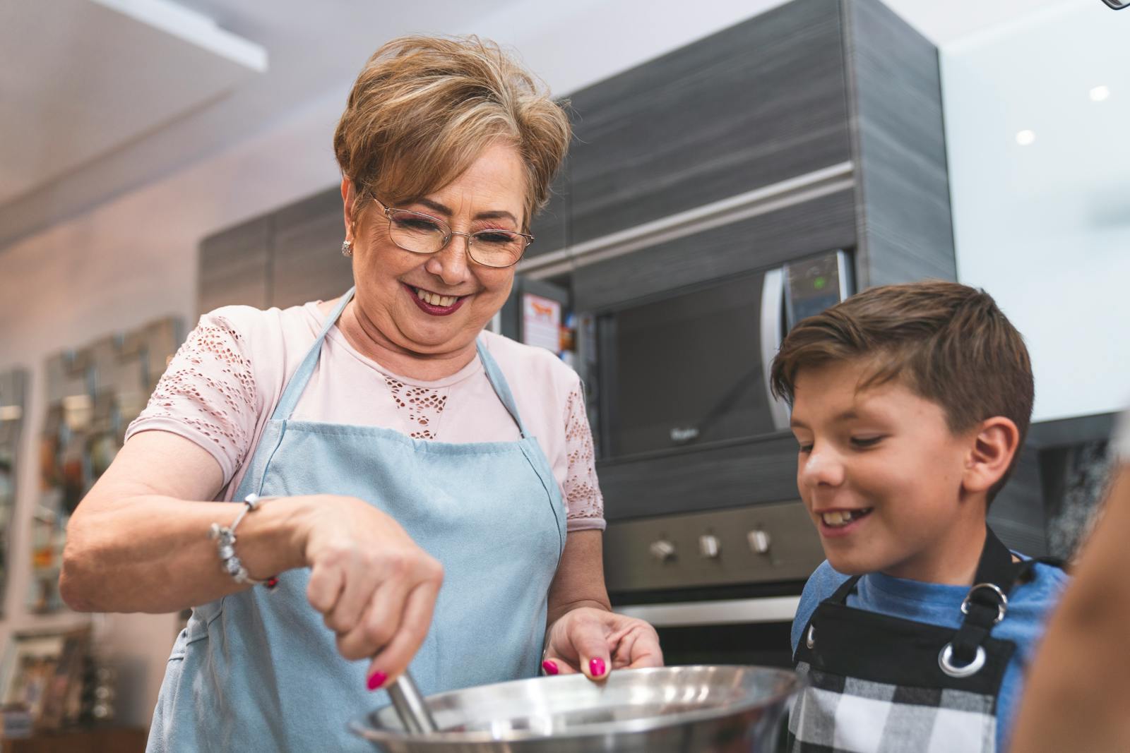 Senior woman and young boy enjoying cooking together in a modern kitchen setting.