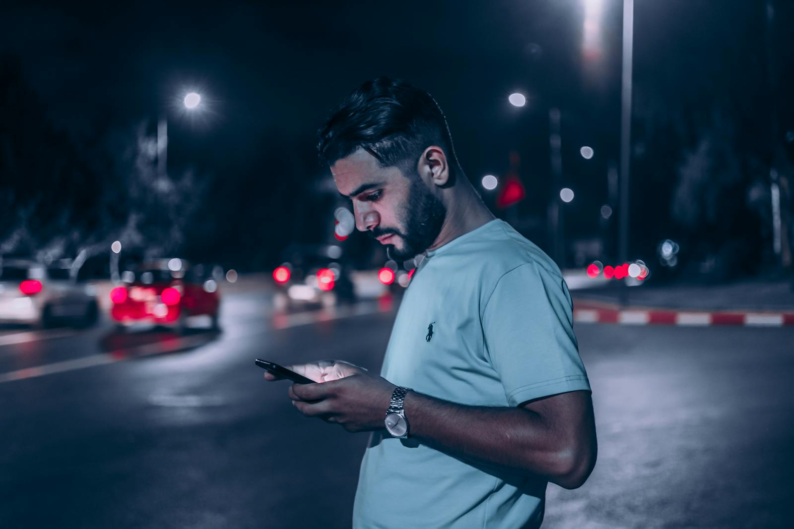 A man in white shirt checks his phone at night on a busy street in Rabat.