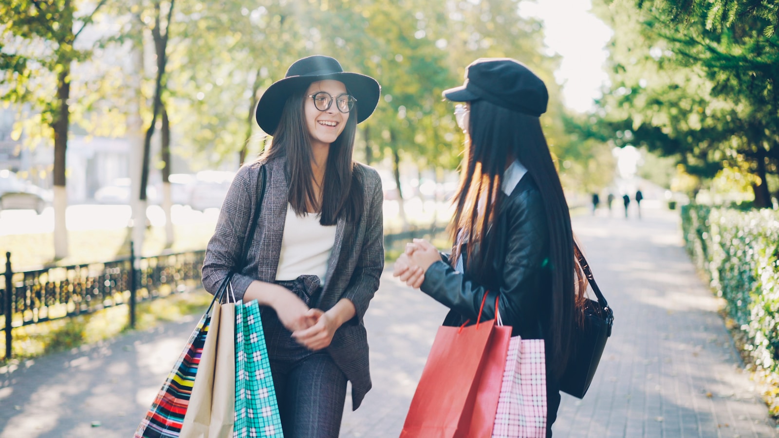 Two women with shopping bags walk outdoors.