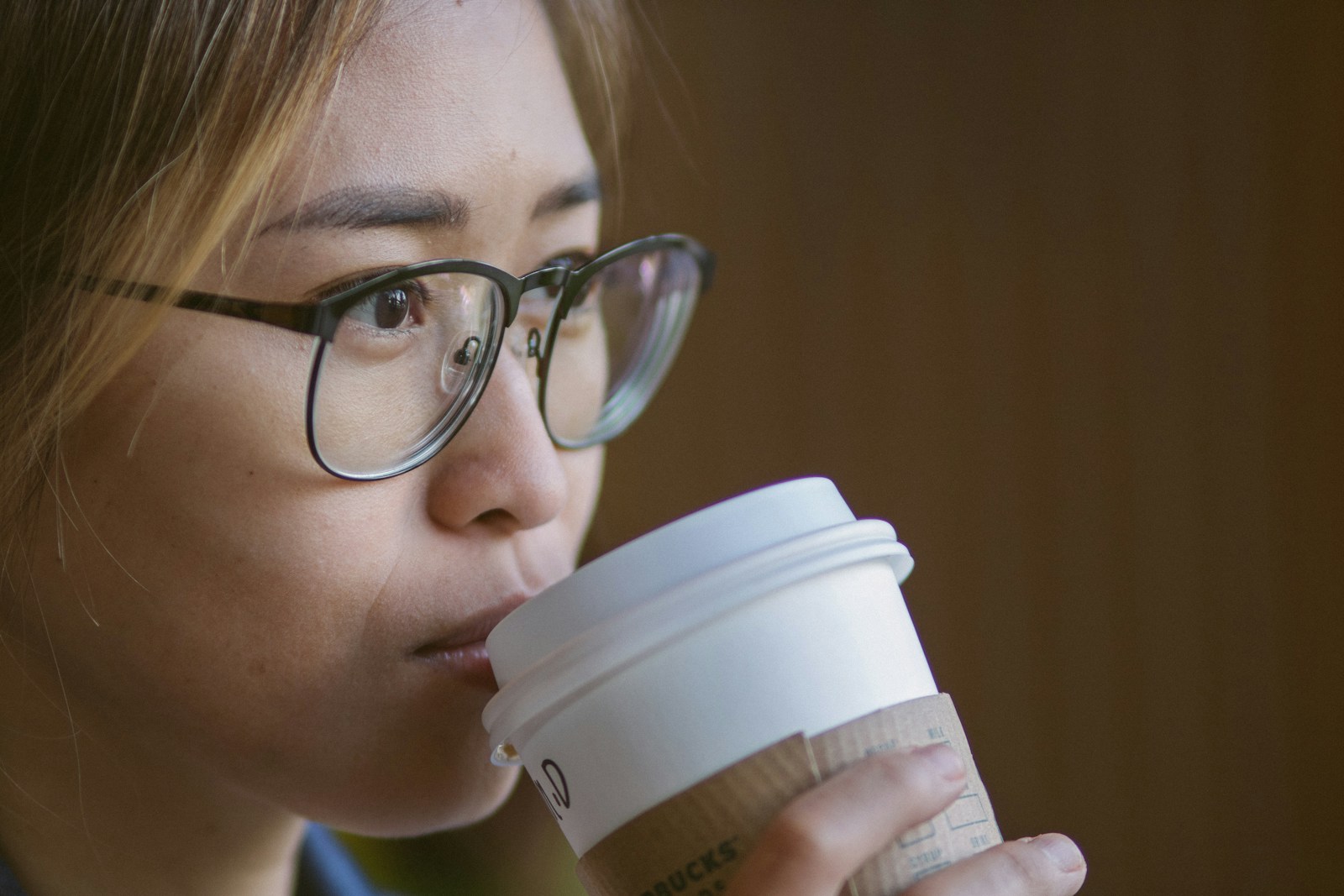 a woman wearing glasses drinking from a coffee cup