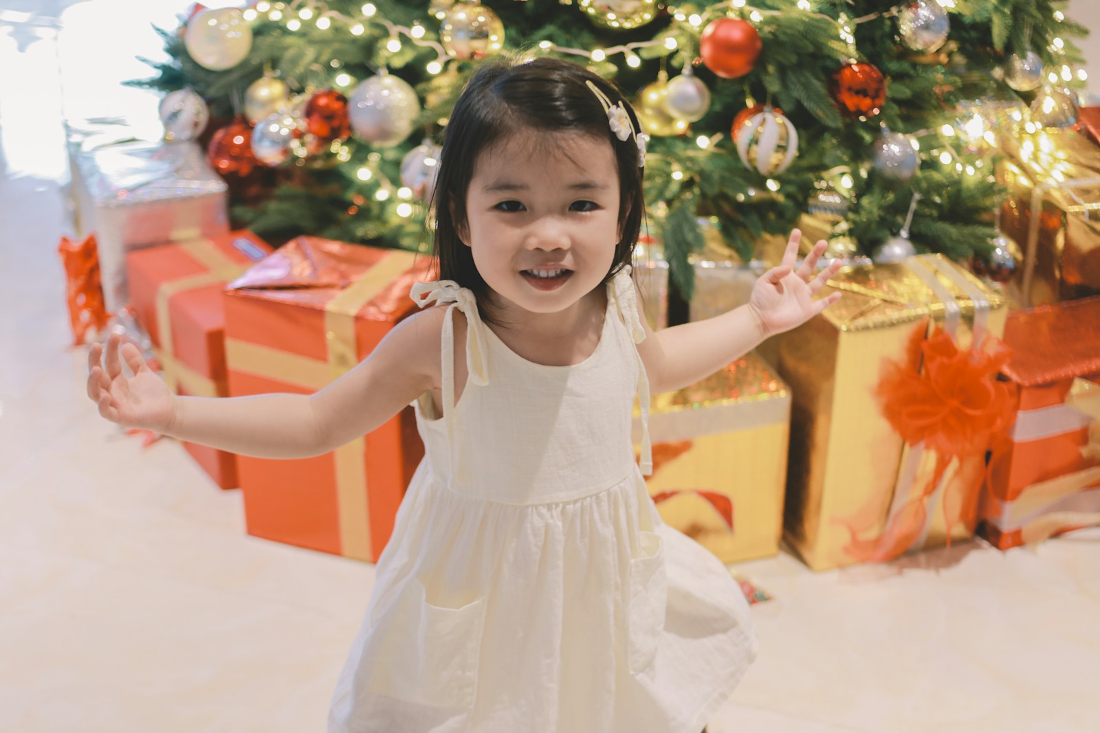 Young girl in white dress with christmas tree and gifts.