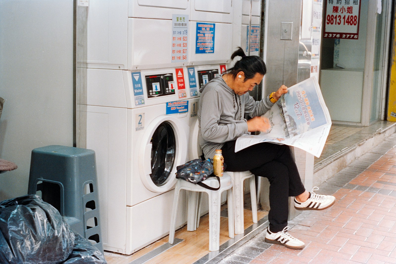 Man reading newspaper while sitting next to washing machines