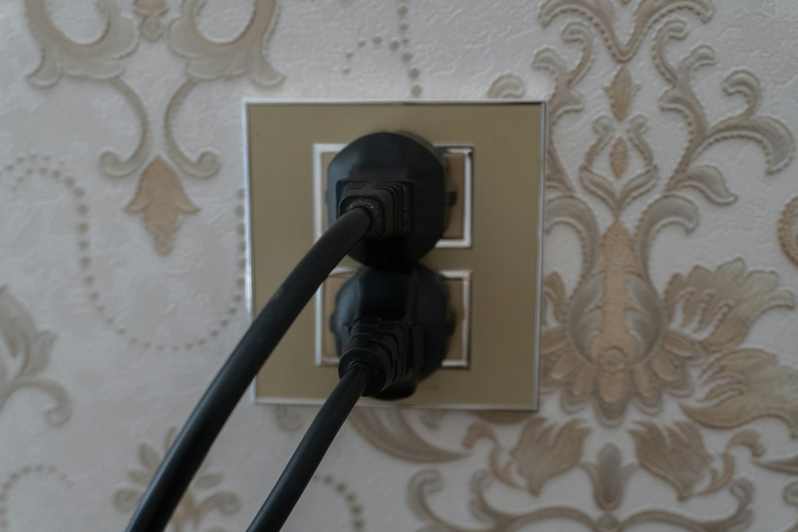 Two black plugs inserted into a gold electrical outlet.