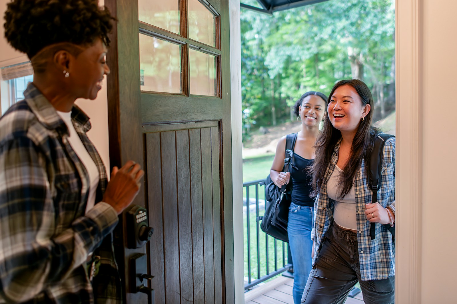 Two women arriving at a doorway, greeted by another woman.