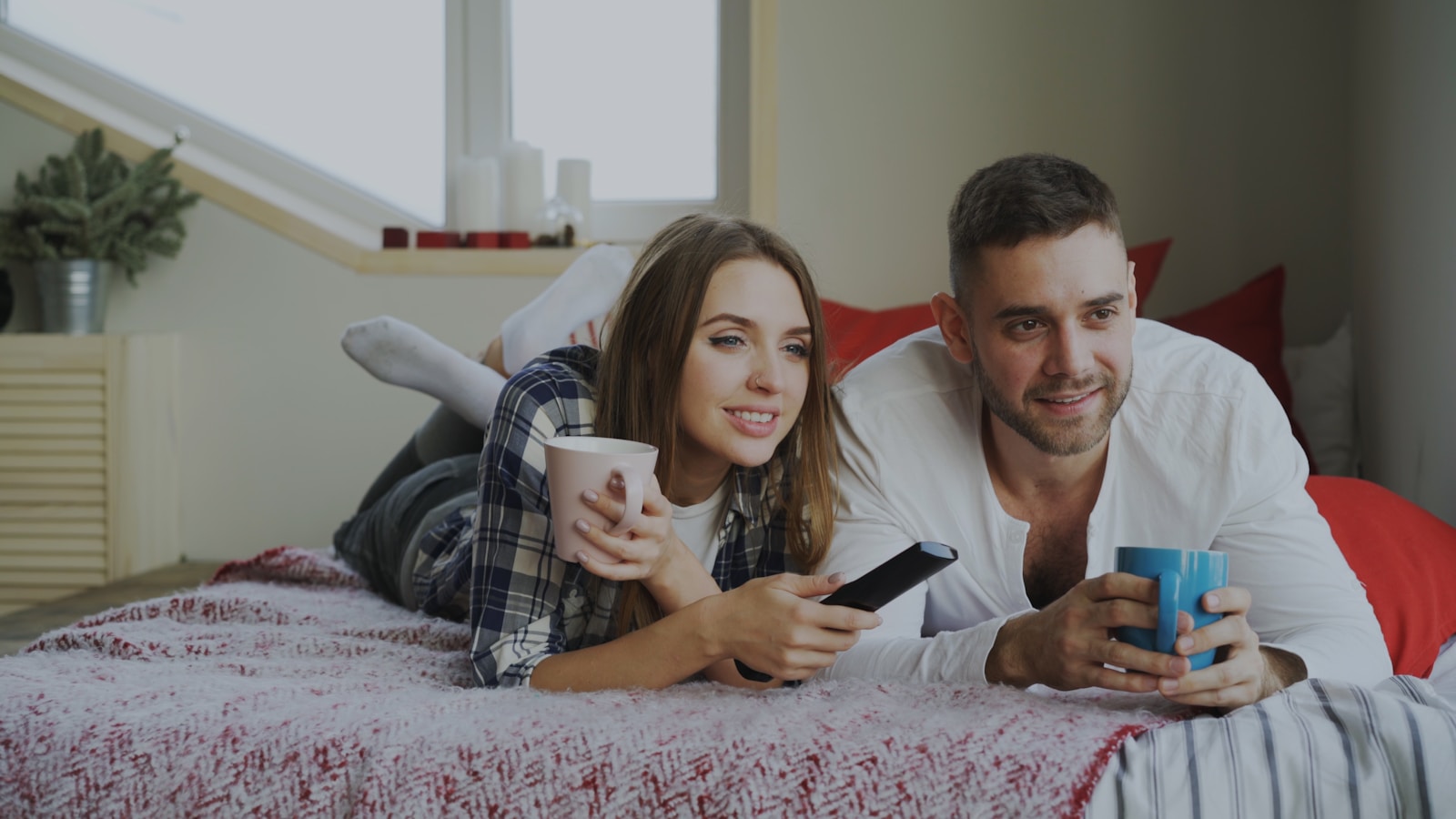 Couple relaxing on bed with coffee and remote.