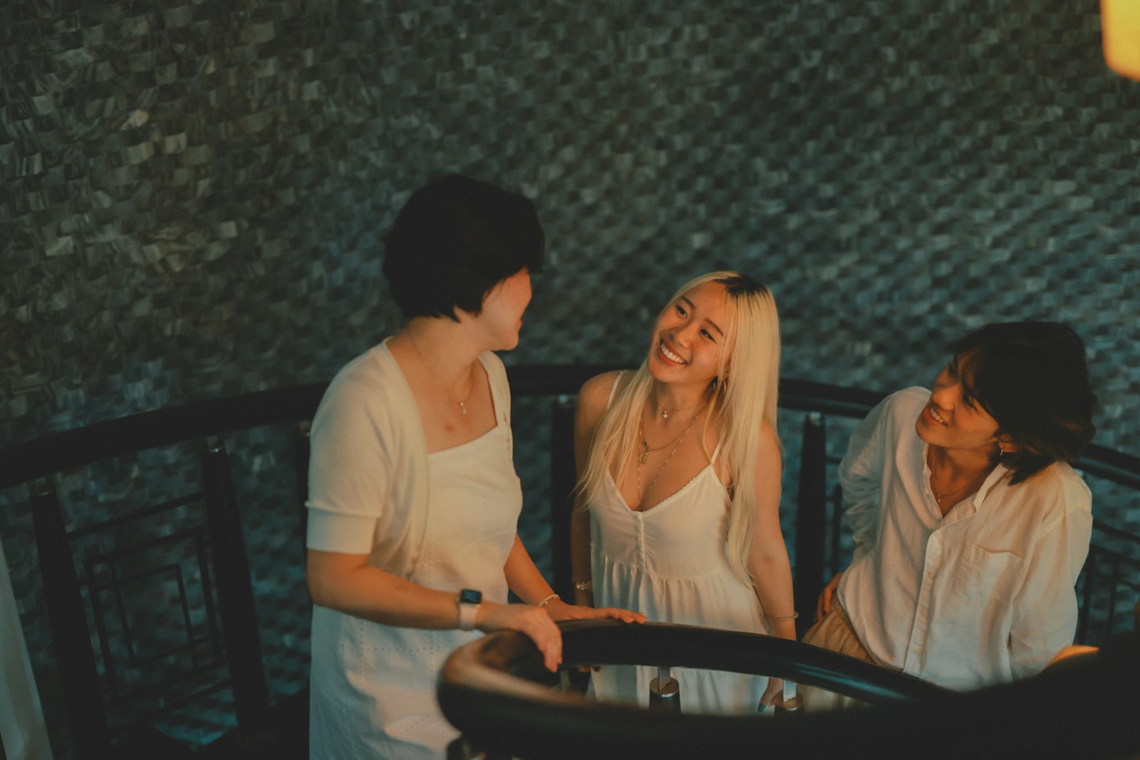 Three women in white outfits talking on stairs
