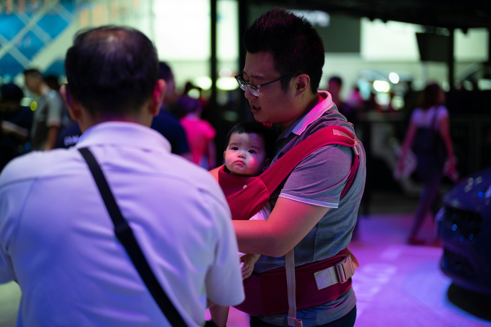 Man carrying baby in a red carrier at an event