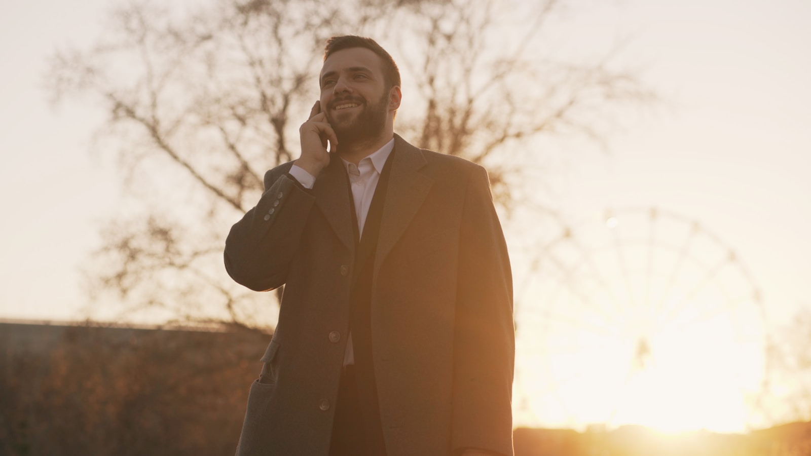 Man in coat talking on phone at sunset