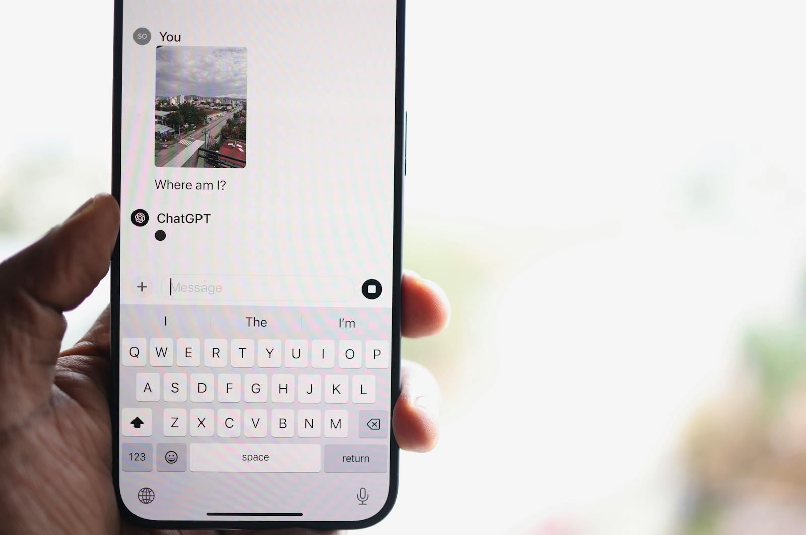 A person holds a smartphone displaying a chat with ChatGPT, inquiring about their location.