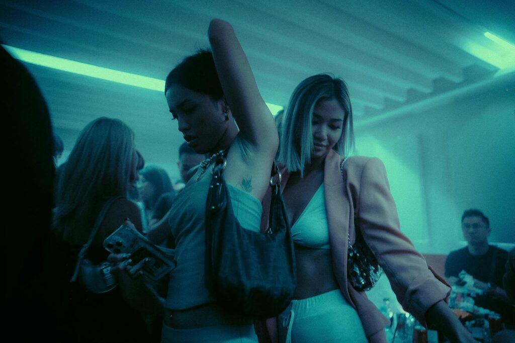 Two women dancing energetically in a lively nightclub with neon blue lighting.