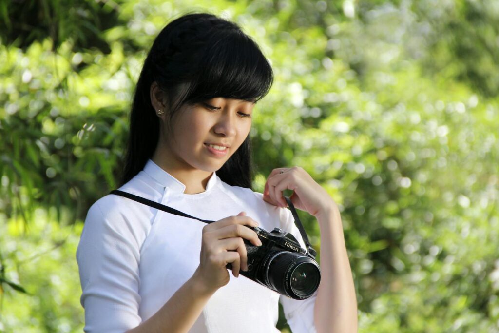 Woman in traditional dress with camera amidst lush greenery in Hoi An.