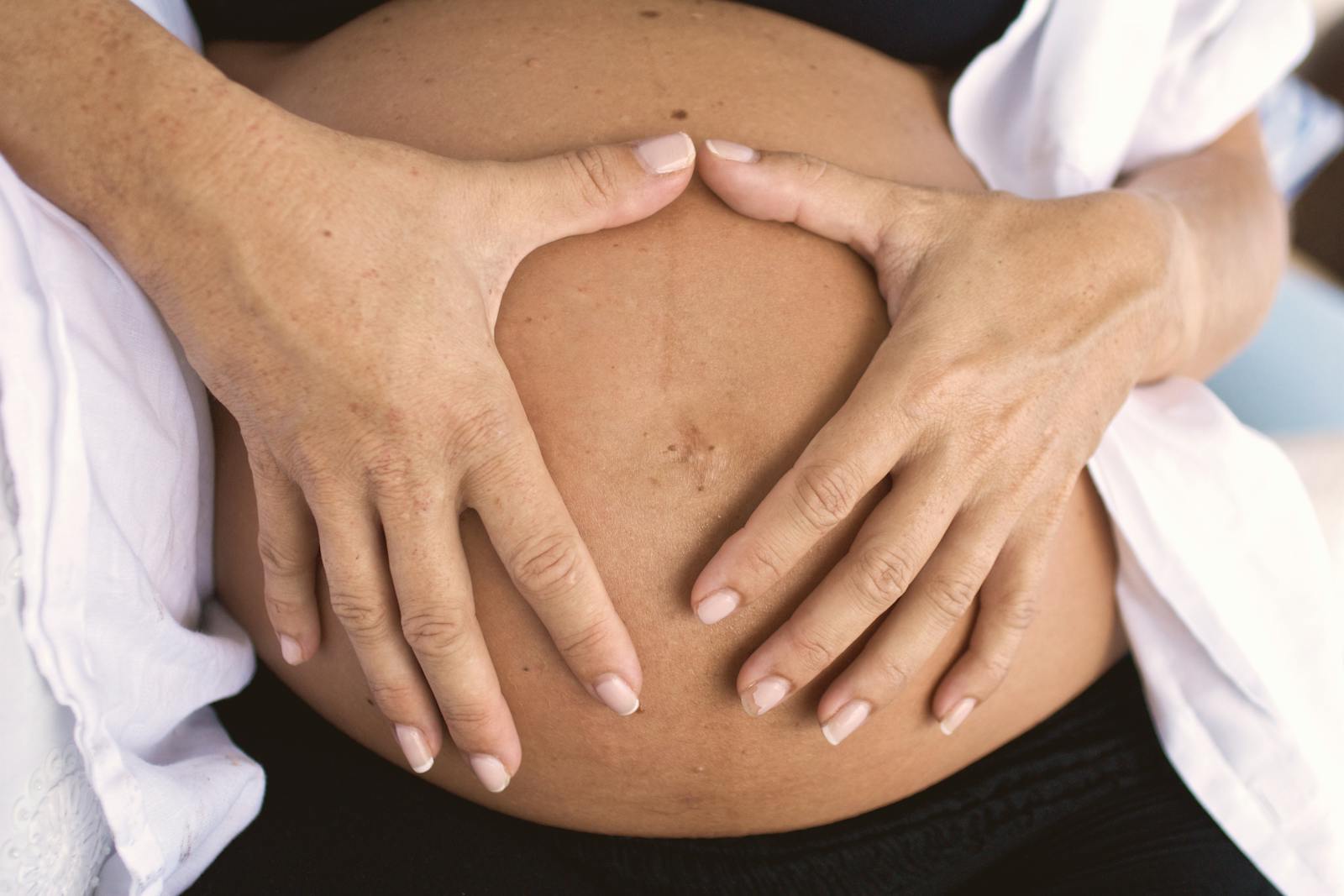 Close-up of a pregnant belly with hands forming a heart shape, symbolizing love and motherhood.
