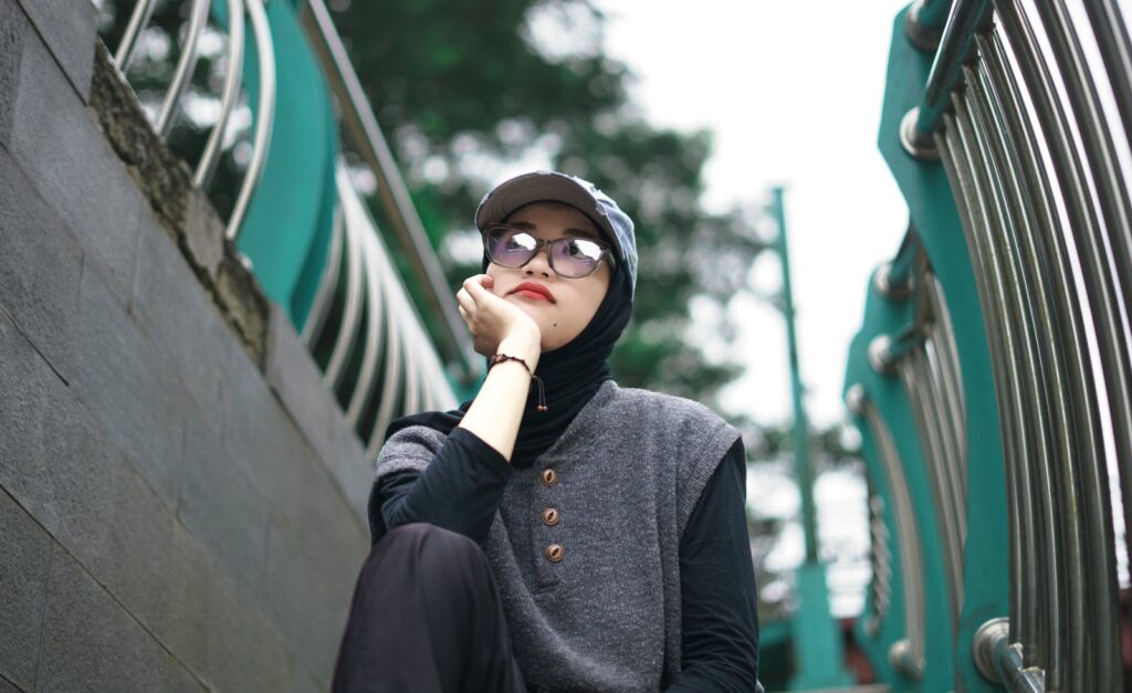 Modern Muslim woman in hijab and glasses posing outdoors on stairs in Banten, Indonesia.