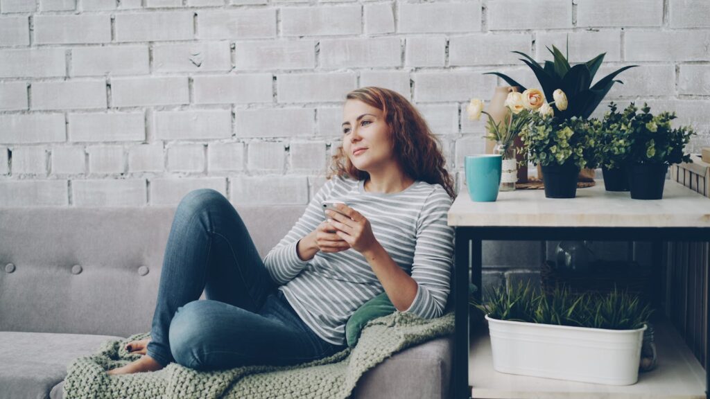 A woman enjoys a relaxing moment on a couch with plants nearby, exuding calm.