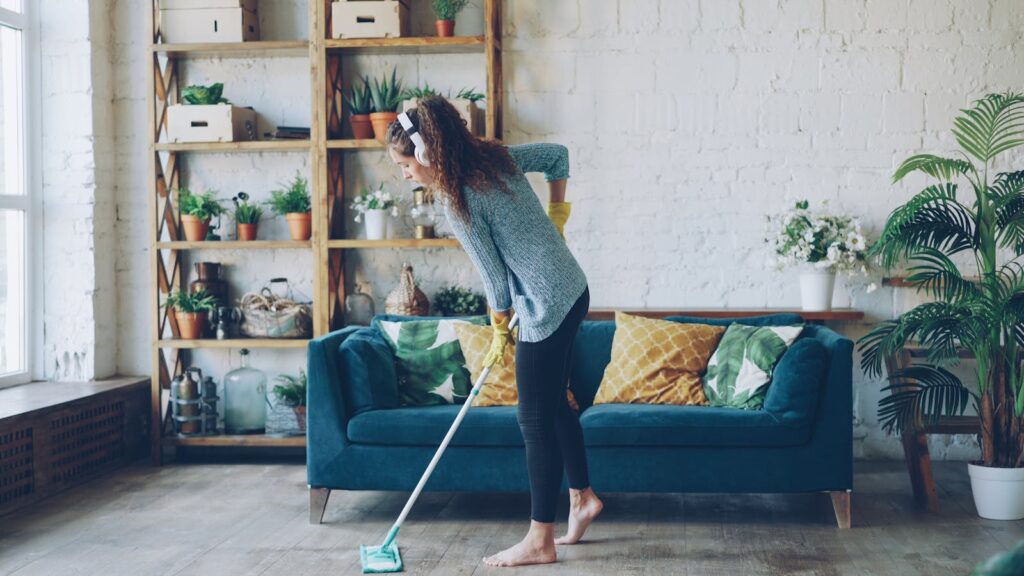 A woman cleaning a stylish living room with a mop, surrounded by plants and decor.