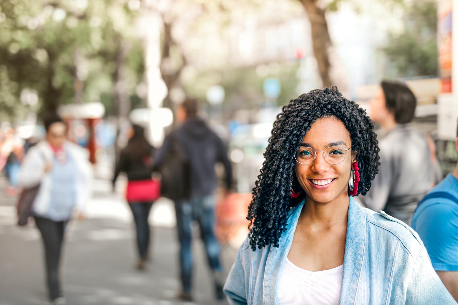 Confident woman smiling on a sunny day amidst a bustling urban street scene.