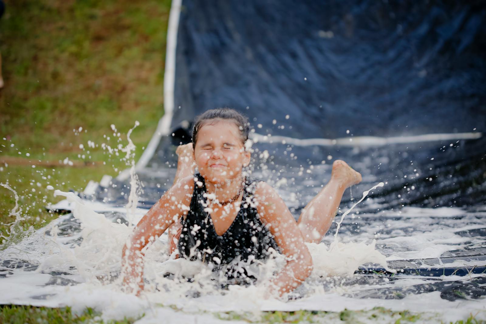 Young girl having fun on a slip and slide in summer, showcasing joy and splash of water.