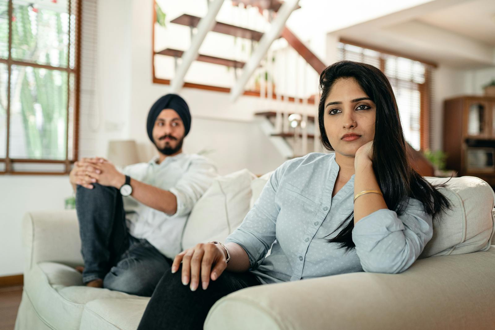 Offended Indian woman sitting on sofa with husband on another end and looking away while having argument