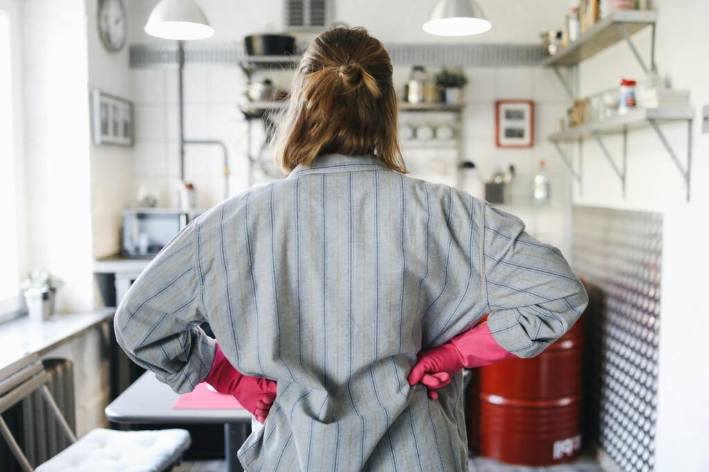 Back view of person wearing pink gloves standing in a cozy kitchen.