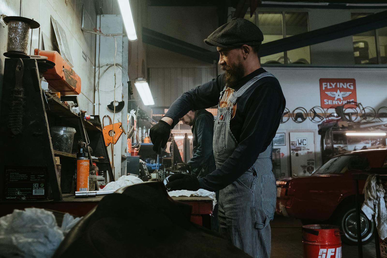 Mechanic performing repairs in a vintage garage setting, using tools and machinery.