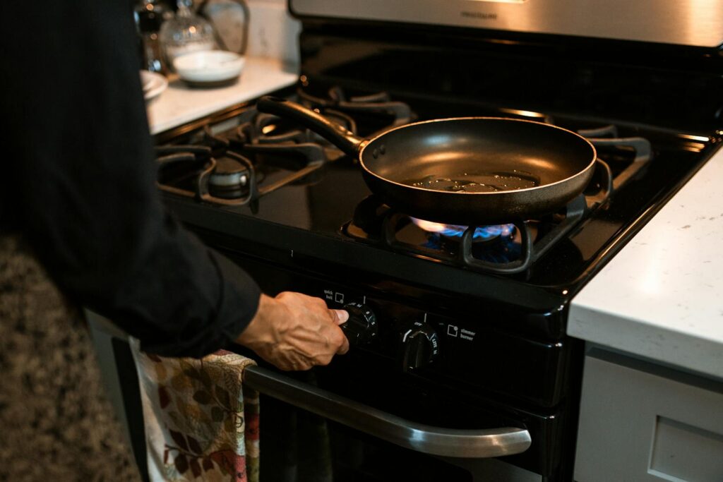 A person in a modern kitchen adjusting the stove dial under a frying pan on a gas burner.