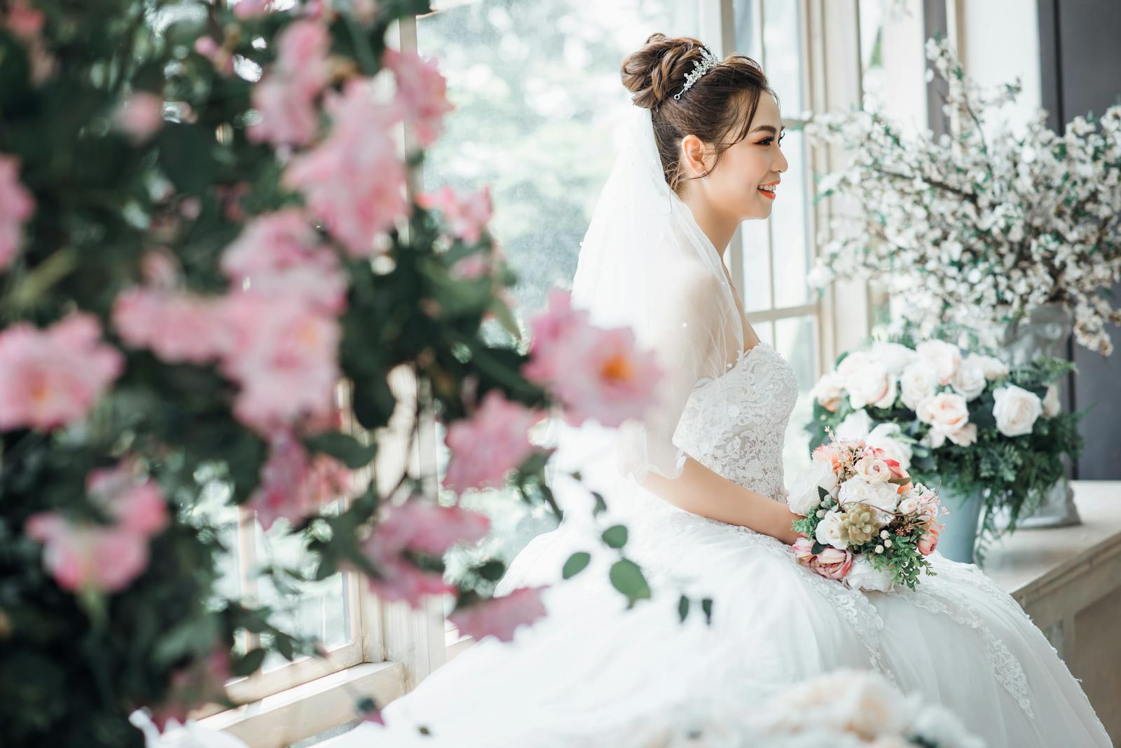 A beautiful bride in a white gown smiles amidst elegant floral arrangements on her wedding day.
