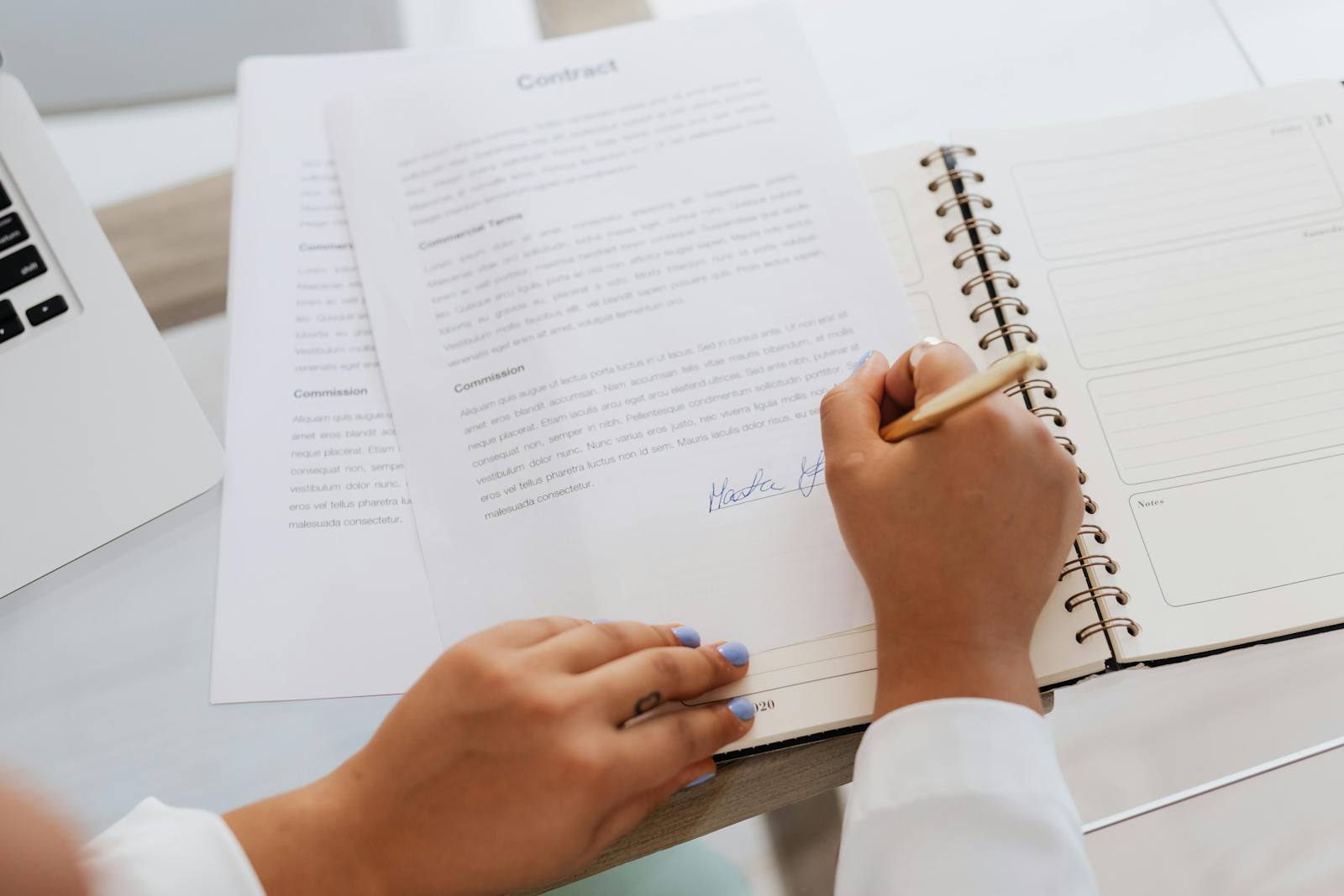 Close-up of hands signing a contract on a desk with office supplies, symbolizing legal agreements.