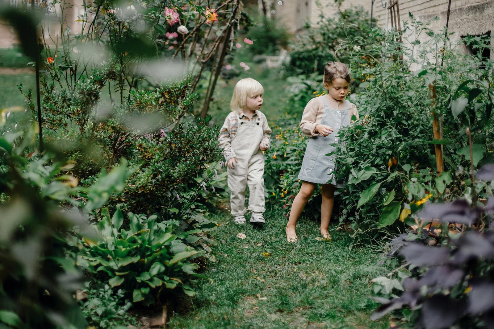 Two children explore a lush home garden, surrounded by vibrant greenery and flowers.