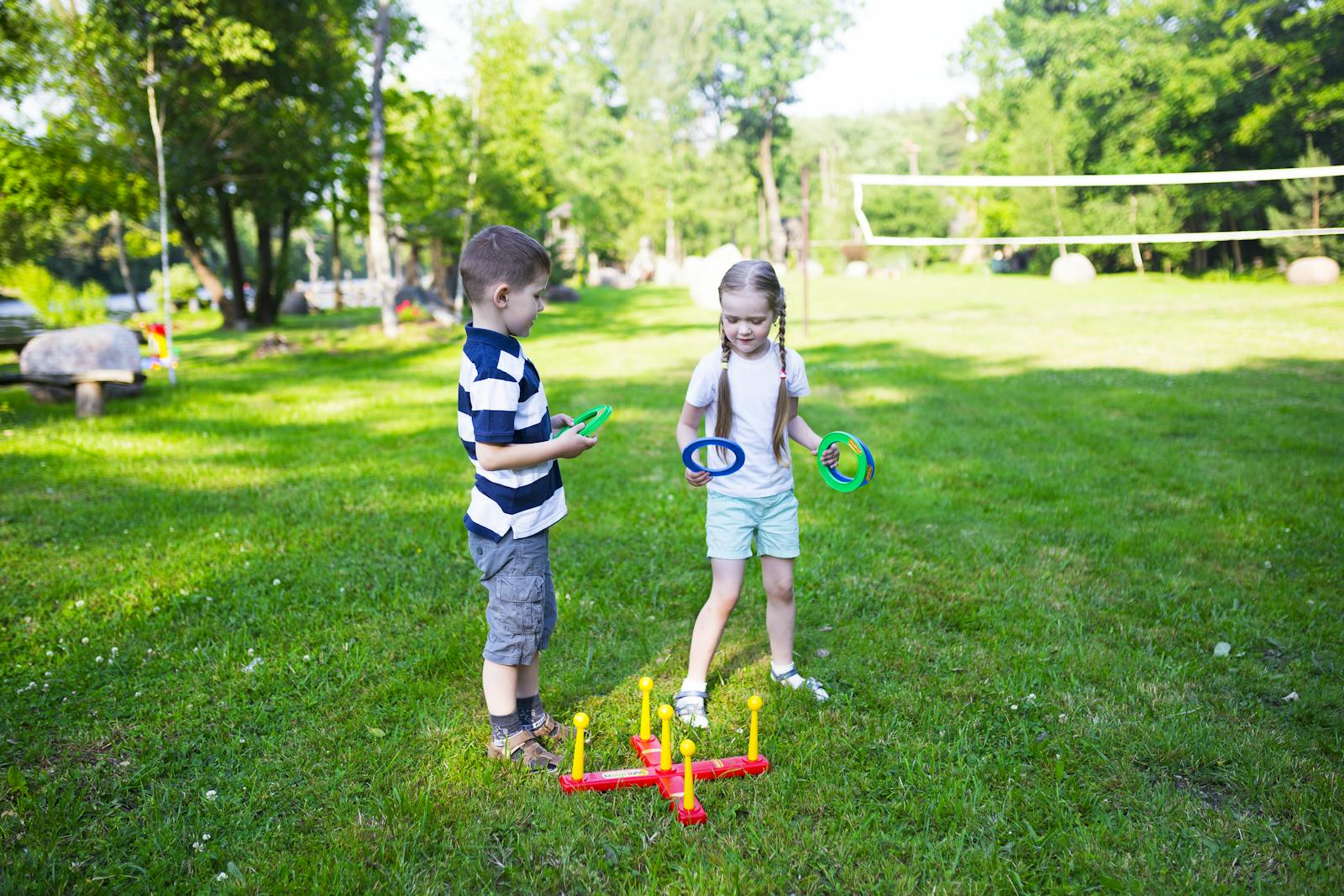 Two kids enjoying a ring toss game outdoors in a sunny park setting.