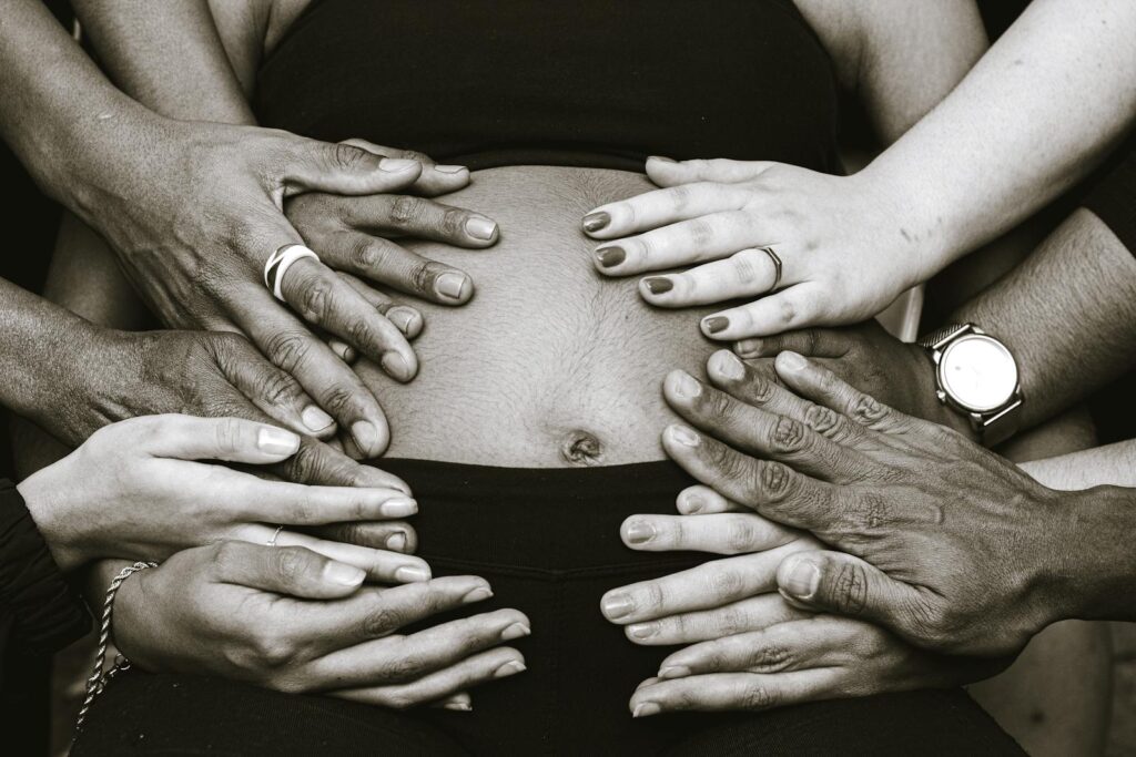 Black and white hands of anonymous multiracial people touching bare belly of faceless pregnant woman while anticipating birth of baby