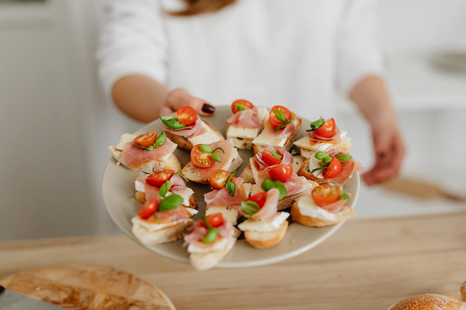 Close-up of a plate with canapés topped with prosciutto, cheese, and cherry tomatoes.