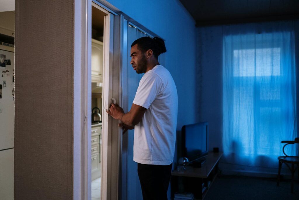 Man in a white shirt opening a door in a dimly lit room, creating a moody atmosphere.