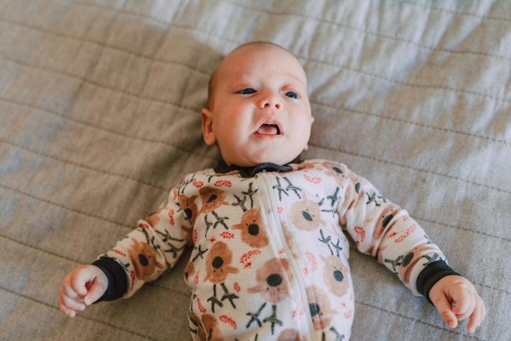 Cute baby in a floral onesie lying on a bed, showcasing innocence and joy.