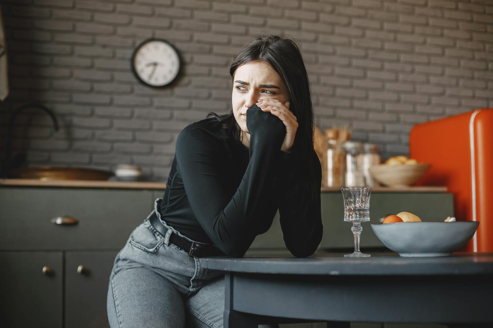 Young woman in a pensive mood, sitting indoors with a clock in the background.