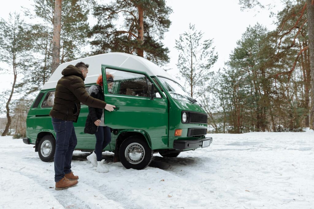 A couple enjoying a winter road trip in a classic green camper van amidst a snowy forest landscape.