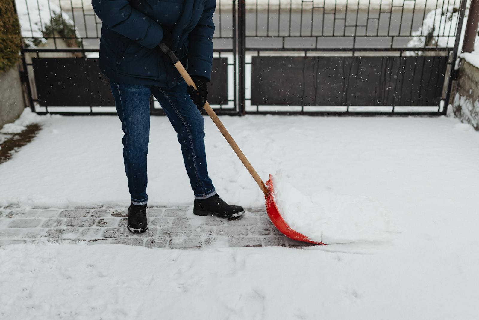 A person shoveling snow on a paved path during a winter day, wearing warm clothing.