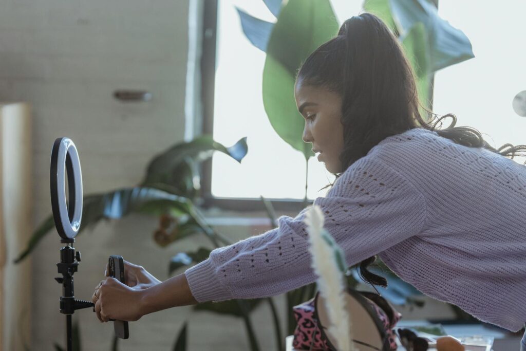 Focused young woman adjusts smartphone tripod for video shoot indoors.